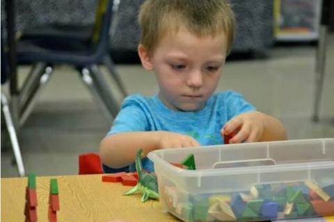 小男孩在课桌前整理积木，面前放着积木的塑料箱