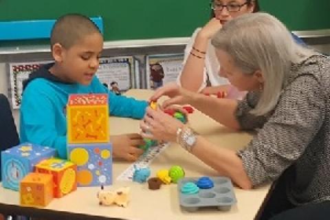 一位母亲在照顾者技能培训工作坊中与患有自闭症的孩子一起工作。照片由Mom2Mom