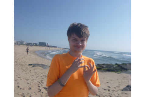 一个穿着橙色衬衫的年轻人站在沙滩上看着镜头