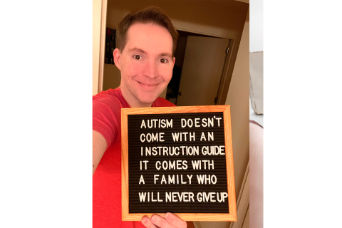 一名穿着红色衬衫的男子举着一块写着“自闭症并没有指导指南，它来自一个永不放弃的家庭”的纸板。