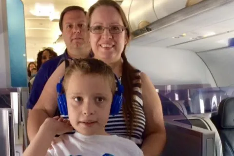 一个男孩和爸爸妈妈一起上飞机，男孩戴着蓝色的耳机